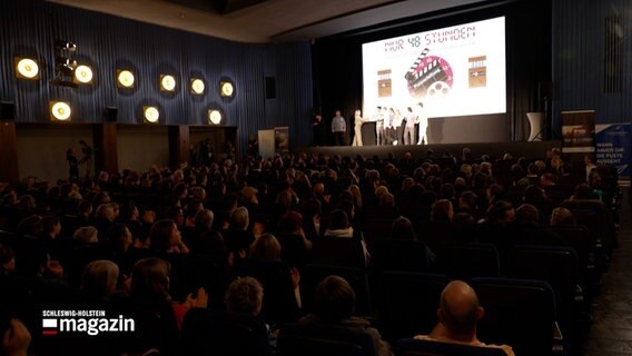 Mehrere Personen gehen von einer Bühne, auf der Bühne wird über einen Projektor das Logo des Filmwettbewerbes "Nur 48 Stunden" gezeigt © NDR Foto: NDR Screenshot