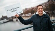 Podcaster Mario Neumann steht mit einem Schild "eine Stunde reden" auf einer Brücke in Bremen. © Radio Bremen Zwei 